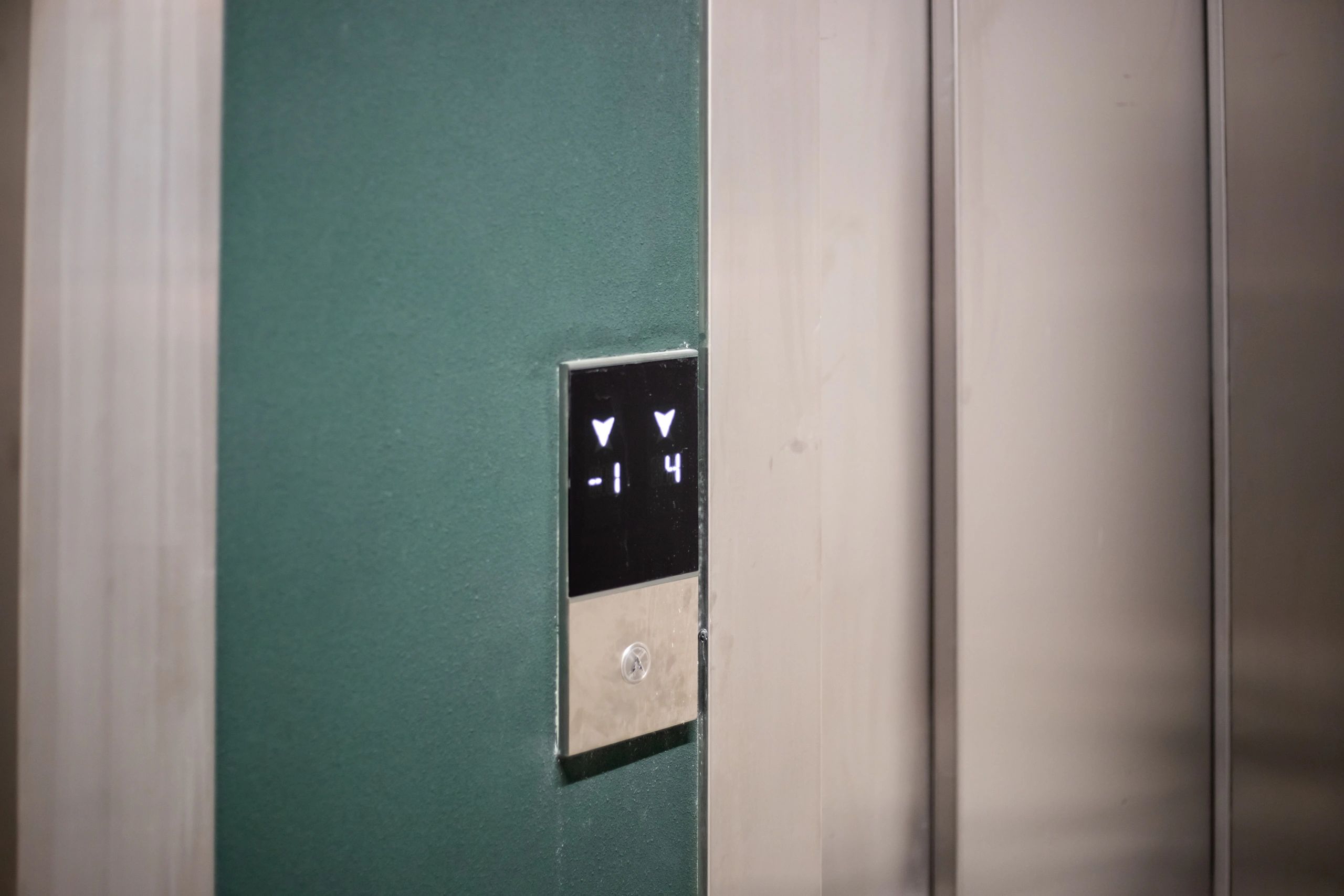 Black-and-white close-up of a modern elevator call panel beside elevator doors